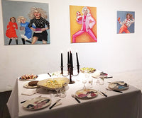 “Milk” by Katrin Valgemäe displayed alongside other artworks in the “Queens of Chaos” exhibition, with a curated dining setup complementing the artistic atmosphere